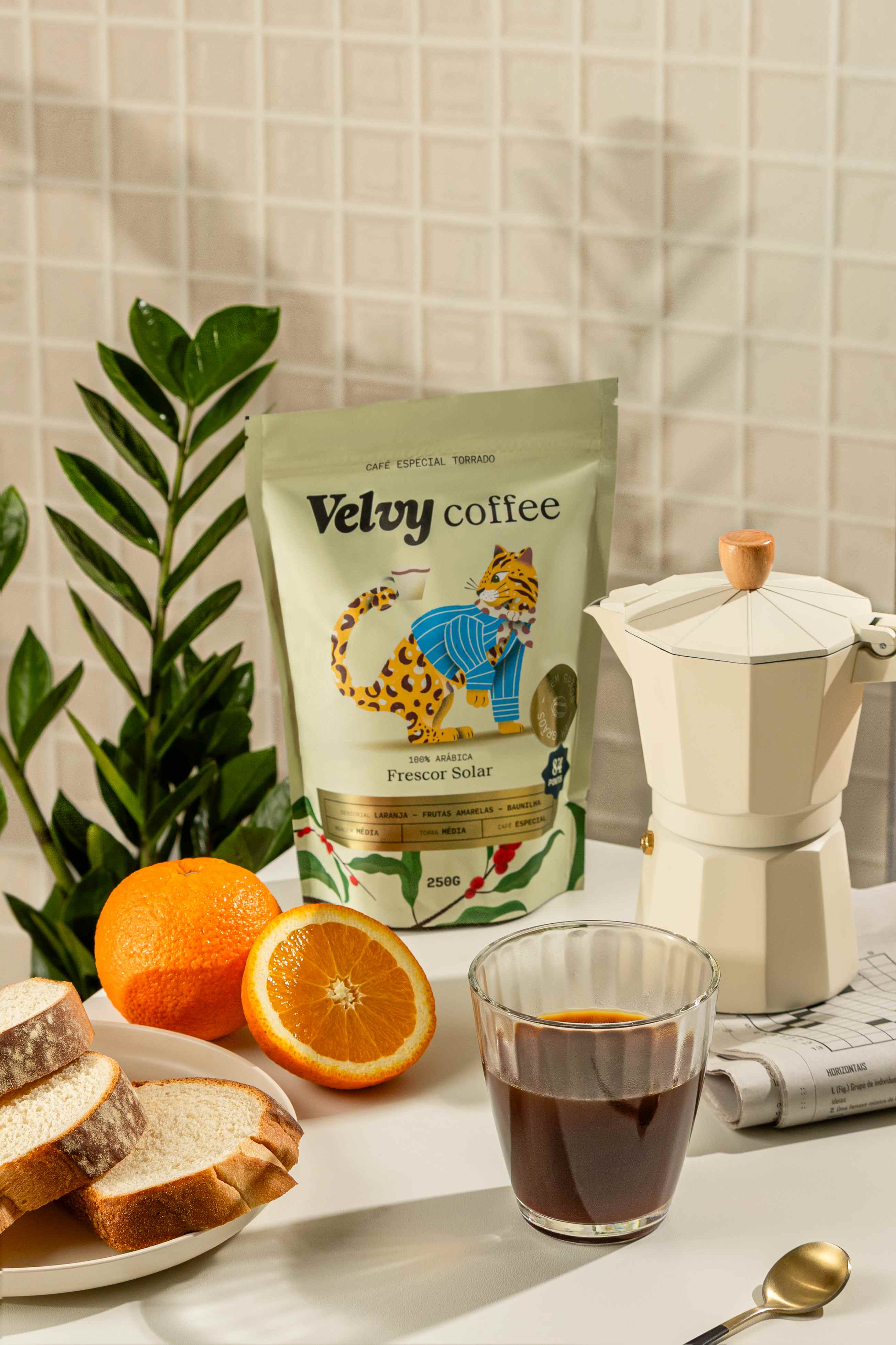 Pacote de café especial ao lado de cafeteira italiana, laranjas e pães